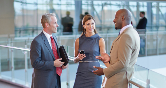 Two men and a woman stand along a glass railing having a discussion.
