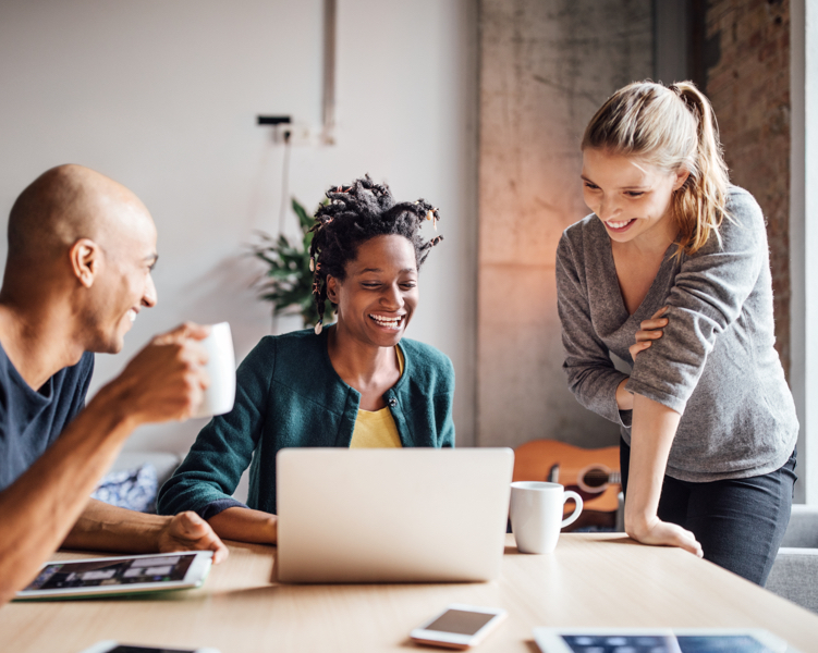 A man and two women at a table looking at a laptop.