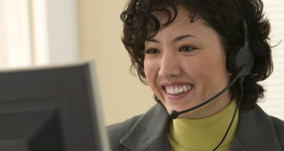 A woman wearing a headset with microphone looks at her computer screen.