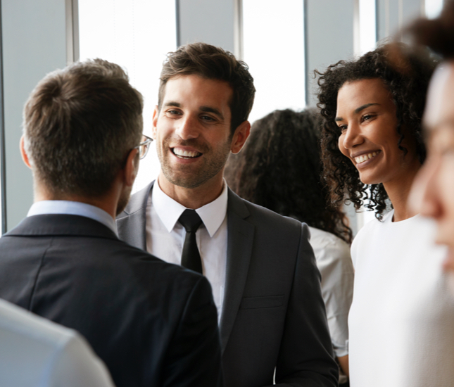 Two college graduates smiling and talking to a man