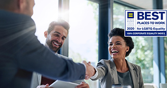 A man and a woman laughing and shaking hands while a third man smiles and watches