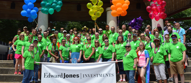 A large group of associates in green t-shirts stand behind an Edward Jones Investment banner.