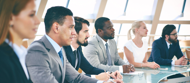 Group of professionals sitting at a conference table, listening.
